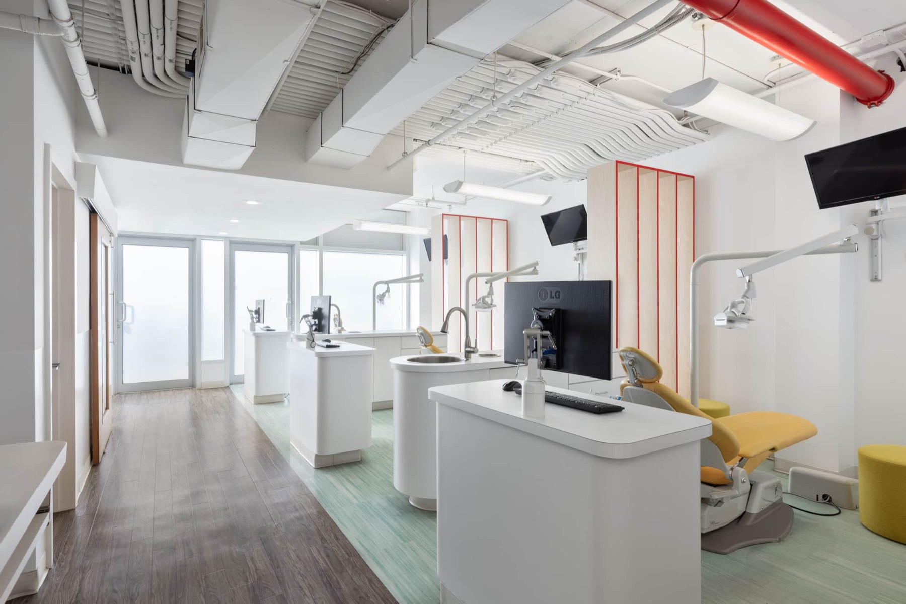 The open hygiene bay at Bitesize Williamsburg, mint green floor, rounded white operatory pods with their own sinks, birch slat dividers and wall mounted screens on articulated arms